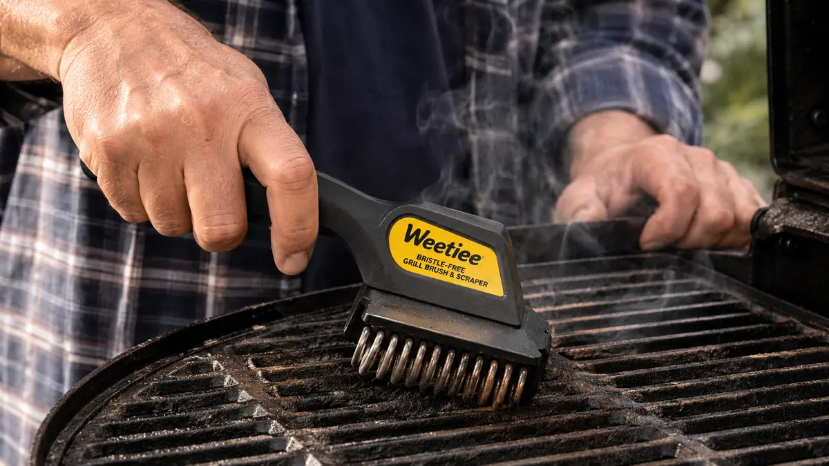Close-up of a stainless coil bristle-free grill brush scrubbing warm cast iron grill grates