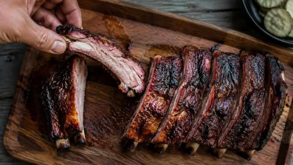 Sliced ribs on a cutting board pulling apart cleanly with a light tug, smoke ring visible along the edge